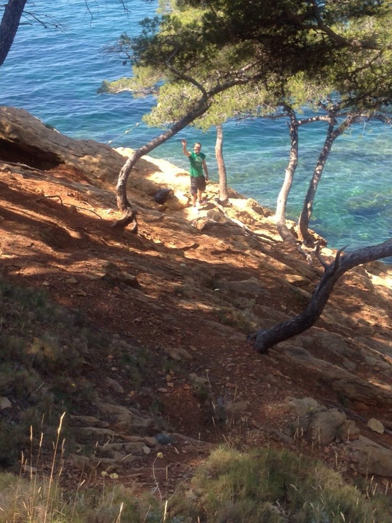 Sentier escarpé descendant vers une calanque de la Côte Bleue entre les pins, au-dessus d'une eau turquoise.