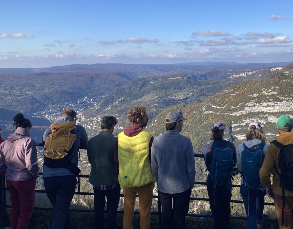 Group of hikers seen from behind, facing a limestone cirque in the Haut-Jura in autumn.